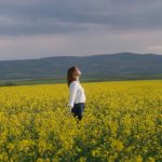 A woman enjoying tranquility in a vibrant yellow canola field under a cloudy sky in Merzifon, Türkiye.