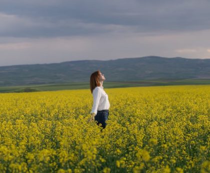 A woman enjoying tranquility in a vibrant yellow canola field under a cloudy sky in Merzifon, Türkiye.