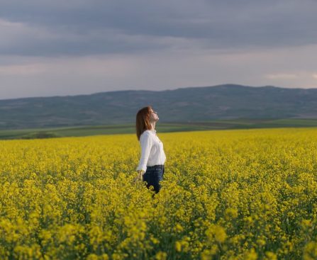 A woman enjoying tranquility in a vibrant yellow canola field under a cloudy sky in Merzifon, Türkiye.
